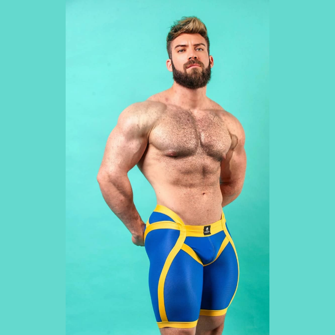 Unieke blauwe short met verlaagde tailleband aan de voorzijde en gele elastische banden, ontworpen door het Italiaanse modehuis Sparta’s Harness en te koop bij Flavourez.