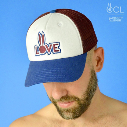 Wit, rood, blauwe truckers cap van Cartoon Called Life voorzien van 'Love' borduursel. Perfect voor gay mannen en verkrijgbaar bij Flavourez